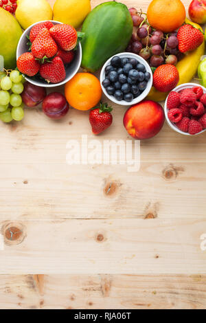 Fröhlich bunte Früchte Beeren, Erdbeeren, Orangen, Pflaumen Trauben mango Papaya rote Johannisbeeren Pfirsiche auf Holztisch, Ansicht von oben, Kopieren, selektive Stockfoto