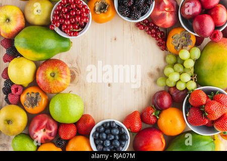 Rainbow Früchte Hintergrund Kreis Rahmen, Pflaumen Erdbeeren Himbeeren Orangen, Äpfel, Kiwis, Weintrauben, Heidelbeeren mango Kaki auf hellem Holz Tisch Stockfoto