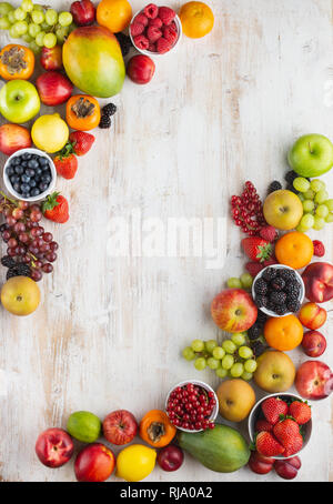 Rainbow Früchte Hintergrund Rahmen, Pflaumen Erdbeeren Himbeeren Orangen, Äpfel, Kiwis, Weintrauben, Heidelbeeren mango Kaki auf weißem Holz- Tabl Stockfoto