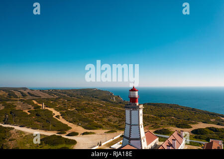 Antenne; drone Ansicht der weiß-roten Leuchtturm Cabo Espichel am Rande der Erde, türkisfarbenen Wasser des Atlantischen Ozeans erstreckt sich bis zum Horizont; schöne Stockfoto