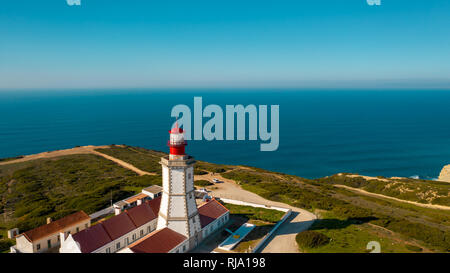 Antenne; drone Ansicht der weiß-roten Leuchtturm Cabo Espichel am Rande der Erde, türkisfarbenen Wasser des Atlantischen Ozeans erstreckt sich bis zum Horizont; schöne Stockfoto