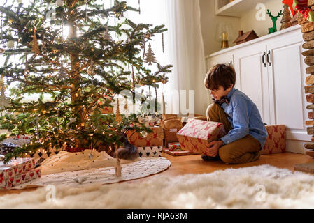 Junge kniend vor einem Weihnachtsbaum, Geschenke Stockfoto