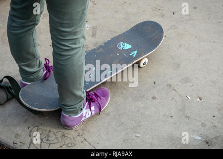 Eine weibliche skater Tragen von Hosen und Trainer steht über ihr Skateboard auf der Ebene Skatepark in Brighton, East Sussex, UK. Stockfoto