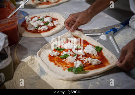 Vorbereitung Pizza Margherita auf einem Marmor Arbeitsplatten. Pizzaiolo setzt Pizza Teig auf die Schale. Selektiver Fokus Stockfoto