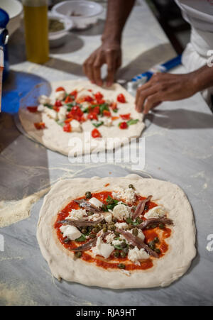 Vorbereitung Pizza Margherita auf einem Ablageflächen aus Marmor. Neapolitanische Pizza, mit anchoives und Kapern, im Vordergrund. Selektiver Fokus Stockfoto