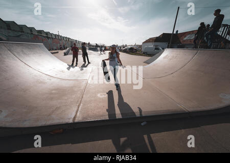 Halten Sie Ihr Skateboard ein junges Mädchen aus geht eine Rampe an der Hove Lagune Skatepark in Hove, Brighton, England. Stockfoto