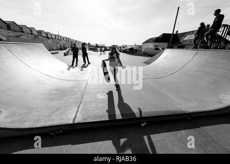 Halten Sie Ihr Skateboard ein junges Mädchen aus geht eine Rampe an der Hove Lagune Skatepark in Hove, Brighton, England. Stockfoto