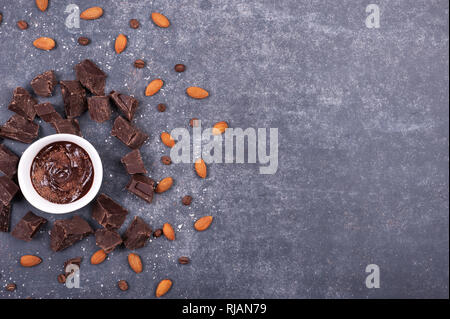 Kreative Gestaltung aus Schokolade Stücke, Tasse mit heißer Schokolade, Kokos Chips und Mandeln auf grauem Hintergrund. Flach. Essen Konzept. Makro Konzept Stockfoto