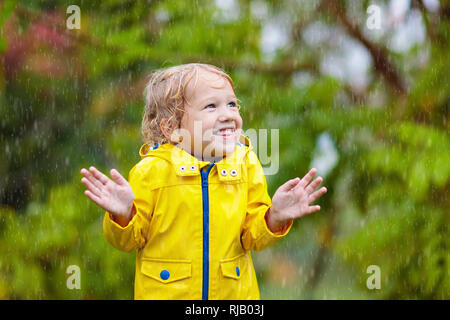 Kinder spielen im Herbst regen. Kinder spielen im Freien an regnerischen Tag. Little Boy fangen Regentropfen unter starken Dusche. Herbst Sturm in einem Park. Wasserdichte Verschleiß Stockfoto