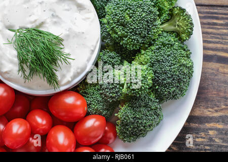 Hausgemachte buttermilk Ranch Salatdressing mit Dill mit frischen Tomaten und Brokkoli über einen rustikalen Holzmöbeln Hintergrund serviert. Bild geschossen über fr Stockfoto