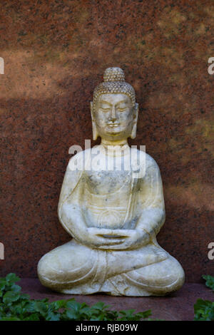 Sitzender Buddha vor einem roten Marmorplatte Stockfoto