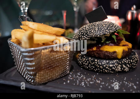Lecker schwarz Burger und Pommes frites im Korb auf dem Schwarzen Brett serviert. Copy-Flag in Bun für Ihren individuellen Text Stockfoto