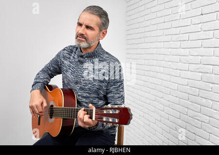 Professionelle Musiker spielen akustische Gitarre und Gesang. Charmanter Mann sitzen und halten Musikinstrumente. Reifen bärtiger Mann im Studio mit weißem Hintergrund posiert. Stockfoto