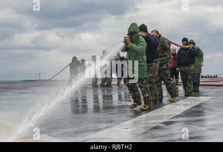 Pazifik (Jan. 13, 2018) Matrosen an Bord der Amphibisches Schiff USS Wasp (LHD 1) ein Flight Deck waschen Verhalten nach einem Wasserfilmbildender Schaum (AFFF) Gegenmaßnahme Wash Down. Wasp ist im Transit zu Sasebo, Japan zu einem Umsatz mit der USS BONHOMME RICHARD (LHD6) als die vorwärts Durchführung bereitgestellten Flaggschiff der amphibischen Kräfte in den USA 7 Flotte Bereich der Operationen. Stockfoto