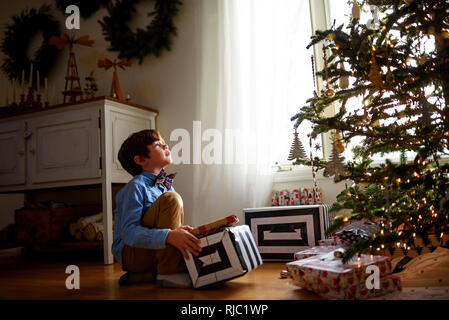 Junge kniend vor einem Weihnachtsbaum, Geschenke Stockfoto