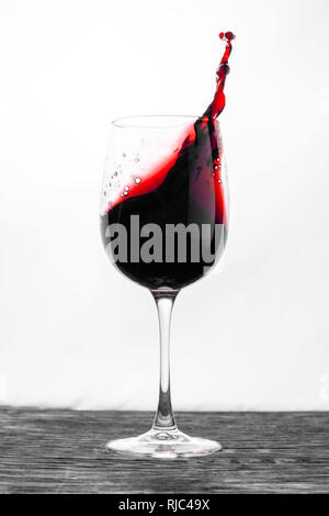 Der rote Wein im Glas spritzt in Bewegung auf einem weißen Hintergrund. Stilvolles Design Karte Stockfoto