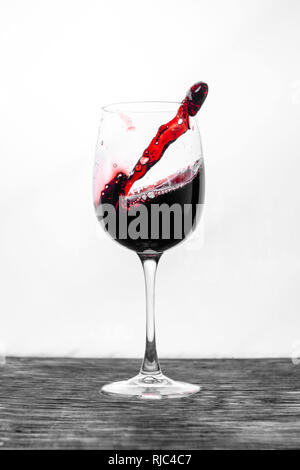 Der rote Wein im Glas spritzt in Aktion auf einem weißen Hintergrund. Stilvolles Design Karte Stockfoto