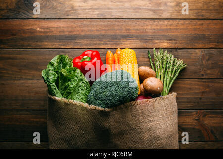 Von oben Leinensack mit verschiedenen frischen Gemüse liegen auf hölzernen Tischplatte Stockfoto