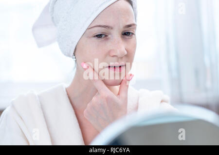 Schöne glückliche junge Frau mit einem Handtuch auf dem Kopf an ihrer Haut in einem Spiegel zu betrachten. Das Konzept der rechtzeitige Hygiene und Pflege für die Haut zu Hause Stockfoto