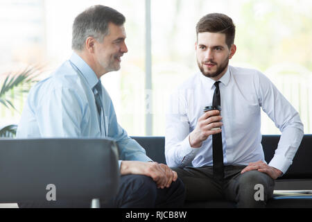 Reifen Geschäftsmann mit einem digitalen tablet Informationen mit einem jüngeren Kollegen in einem modernen Business Lounge zu diskutieren. Stockfoto
