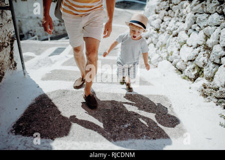 Ein Mittelteil von Vater mit Kleinkind Sohn gehen in der Stadt im Sommerurlaub. Stockfoto