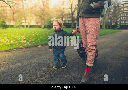 Eine junge Mutter und ihr Kind gehen in den Park mit einem Koffer Stockfoto