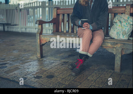 Eine junge Frau sitzt auf einer Bank im Freien und ist trinken Kaffee nehmen Stockfoto