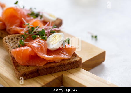 Toast mit geräuchertem Lachs und Wachtelei und Radieschen Sprossen auf rustikalen Holzbrett serviert mit Gläser Weisswein. Köstliche Vorspeise, Snack oder pa Stockfoto