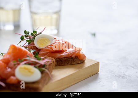 Toast mit geräuchertem Lachs und Wachtelei und Radieschen Sprossen auf rustikalen Holzbrett serviert mit Gläser Weisswein. Köstliche Vorspeise, Snack oder pa Stockfoto