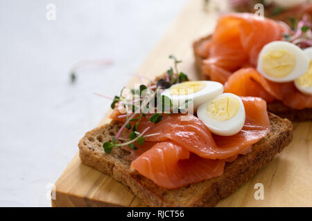 Toast mit geräuchertem Lachs und Wachtelei und Radieschen Sprossen auf rustikalen Holzbrett serviert mit Gläser Weisswein. Köstliche Vorspeise, Snack oder pa Stockfoto