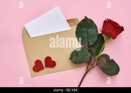 Schreiben Liebe. Beachten Sie Papier mit Umschlag, rote Rose und dekorative Herzen auf rosa Hintergrund. Stockfoto