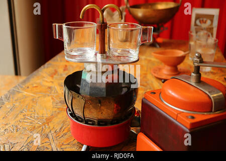 Paar Glas demitasse espresso Tassen auf dem Herd retro mini Kaffeemaschine mit kaffeemühle im Vordergrund Stockfoto