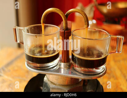 Aromatischer Kaffee heraus rinnt aus Mini retro brauen Topf in ein paar Glas demitasse Cups Stockfoto