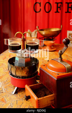 Zwei Tassen frisch gebrühten Espresso auf dem Herd top Retro mini Kaffeemaschine mit mahlwerk im Vordergrund Stockfoto