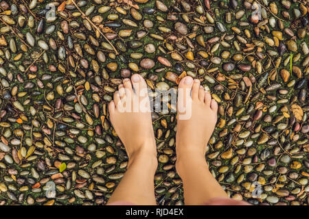 Frau gehen auf eine strukturierte, mit Kopfstein Pflaster, Reflexzonenmassage. Pebble Stones auf dem Bürgersteig für Fußreflexzonenmassage. Stockfoto