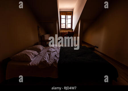 Neue, saubere europäische Doppelzimmer französisches Bett mit Dachschräge und Fenster im Loft mit Tisch und Kissen in dunklen Schlafzimmer Startseite Appartements Zimmer Stockfoto