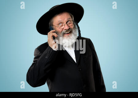 Portrait von alten Senior orthodoxen Hasdim jüdischen Mann mit Handy bei jüdischen Fest Purim im Studio. Die purim, jüdische, Festival, Urlaub, Feier, Judentum, Tradition, Business, Kommunikation, Religion Konzept. Stockfoto