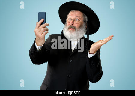 Portrait von alten Senior orthodoxen Hasdim jüdischen Mann mit Handy bei jüdischen Fest Purim im Studio. Die purim, jüdische, Festival, Urlaub, Feier, Judentum, Tradition, Business, Kommunikation, Religion Konzept. Stockfoto