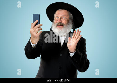 Portrait von alten Senior orthodoxen Hasdim jüdischen Mann mit Handy bei jüdischen Fest Purim im Studio. Die purim, jüdische, Festival, Urlaub, Feier, Judentum, Tradition, Business, Kommunikation, Religion Konzept. Stockfoto