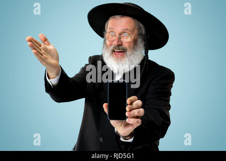 Portrait von alten Senior orthodoxen Hasdim jüdischen Mann mit Handy bei jüdischen Fest Purim im Studio. Die purim, jüdische, Festival, Urlaub, Feier, Judentum, Tradition, Business, Kommunikation, Religion Konzept. Stockfoto