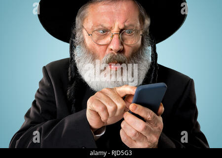 Portrait von alten Senior orthodoxen Hasdim jüdischen Mann mit Handy bei jüdischen Fest Purim im Studio. Die purim, jüdische, Festival, Urlaub, Feier, Judentum, Tradition, Business, Kommunikation, Religion Konzept. Stockfoto