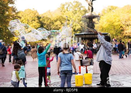 Eine Gruppe von Kindern beobachten ein Mann blasen riesige Seifenblasen im Central Park in New York City, USA. Stockfoto