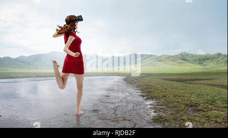 Die Frau im roten Kleid tragen Virtuelle Realität Helm. Mixed Media Stockfoto