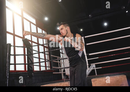 Muskulöse Athleten im Sport Kleidung Üben mit der rechten geraden Schlag in Boxing Gym. Starker junger Mann Schatten tun - Boxen Stockfoto