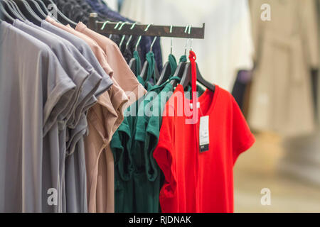 Zeile der neuen farbenfrohen modernen unisex Baumwoll-T-Shirts mit Preisschildern hängen an Rack auf unscharfen Shop Interior Hintergrund. Mode, Verkauf und Einkauf conc Stockfoto