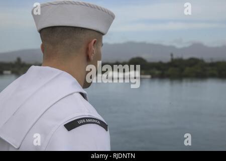 PEARL HARBOR NAVAL BASE, HI - ein Seemann mit dem Amerika Amphibious Ready Gruppe an Bord amphibisches Schiff USS America (LHA 6) die Schienen mans, wie sie das USS Arizona Memorial verlassen, Jan. 25, 2018. Manning der Schienen ist ein Naval Tradition jede Bereitstellung von Schiff führt und ist eine Methode der ehrenkompanie oder Rendering Ehren durch Marineschiffe verwendet. Die 15. MEU und Amerika ARG sind derzeit auf eine Routine für sieben Monate, um die Bereitstellung zu den USA 3., 5. und 7 Flotte Bereiche des Betriebes als Reaktion auf Krisen und Kontingenz Kraft eingesetzt. Stockfoto