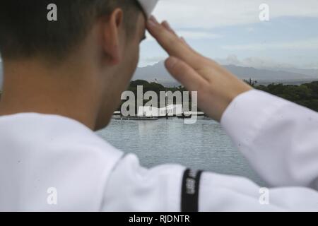 PEARL HARBOR NAVAL BASE, HI - ein Seemann mit dem Amerika Amphibious Ready Gruppe an Bord amphibisches Schiff USS America (LHA 6) begrüßt, da sie das USS Arizona Memorial verlassen, Jan. 25, 2018. Manning der Schienen ist ein Naval Tradition jede Bereitstellung von Schiff führt und ist eine Methode der ehrenkompanie oder Rendering Ehren durch Marineschiffe verwendet. Die 15. MEU und Amerika ARG sind derzeit auf eine Routine für sieben Monate, um die Bereitstellung zu den USA 3., 5. und 7 Flotte Bereiche des Betriebes als Reaktion auf Krisen und Kontingenz Kraft eingesetzt. Stockfoto