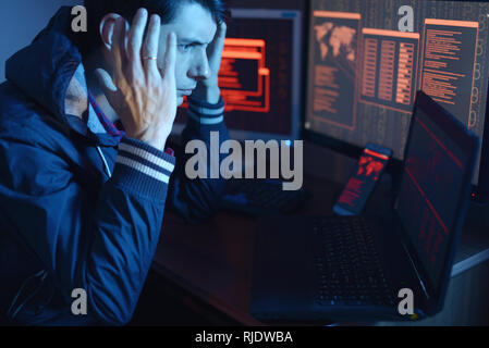 Eine männliche Hacker Gedanken über das Problem der Hacking oder malware Infektion auf dem Hintergrund von Bildschirmen mit Codes im Neonlicht. Das Konzept der cyberse Stockfoto
