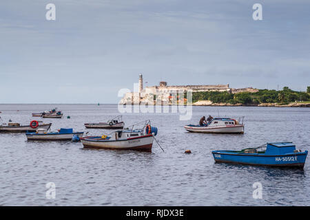Blick auf die Fischerboote mit zwei Fischern und Morro Castle Leuchtturm (Castillo De Los Tres Reyes del Morro) quer über die Bucht von Havanna in Kuba Stockfoto
