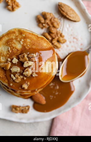 Close-up Stapel amerikanische Pfannkuchen mit Karamell souse und Muttern mit Löffel an der Platte. Makro. Konzept der Frühstück für Kinder. Ansicht von oben Stockfoto